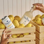 a person holding a bottle of lemonade in front of a crate of lemons