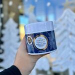 a person holding a cup of whipped cream in front of a christmas tree